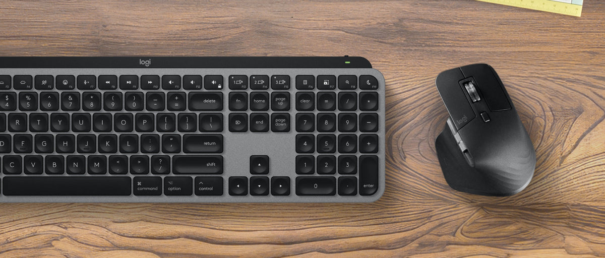 Logitech wireless keyboard and mouse set on a wooden desk, with a small notepad visible in the top right corner.